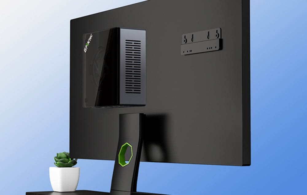 mini PC attached to the back of a black monitor on a blue background